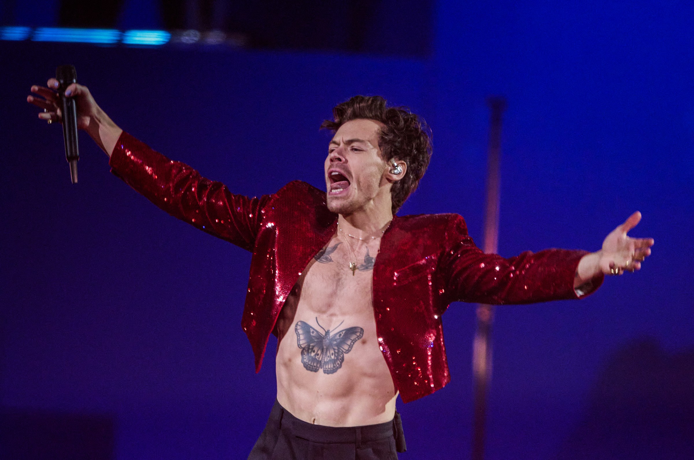 Styles wearing a sparkly red jacket and no shirt onstage