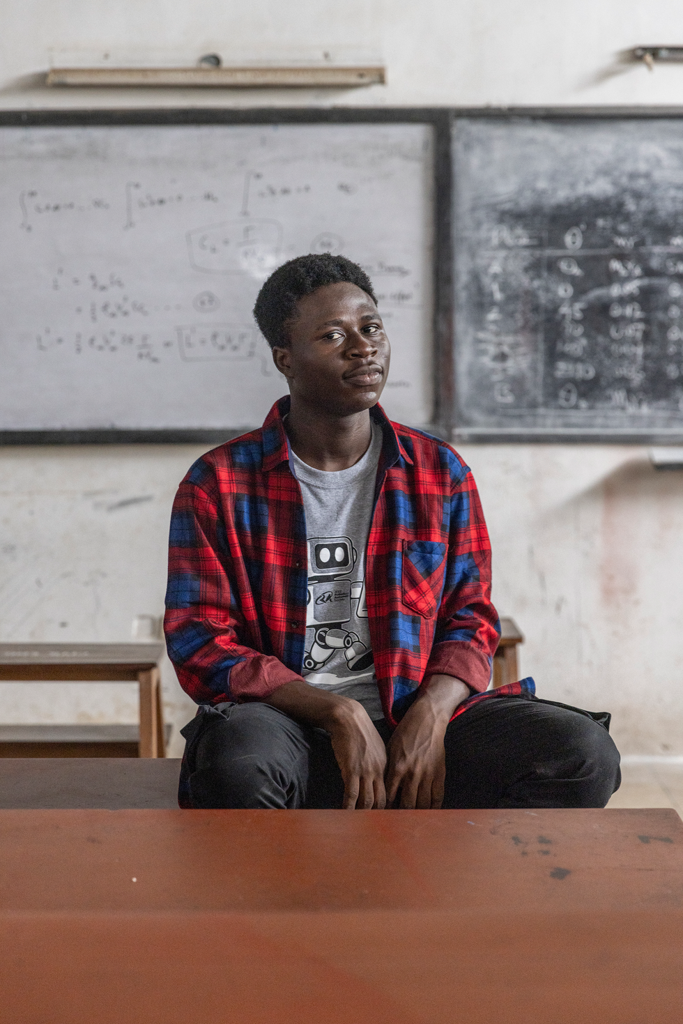 Young Black man in plaid shirt sitting on a chair in front of a white board and a black board