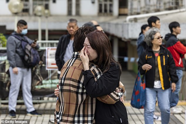 A woman is seen crying near residential buildings that continue to burn at Wang Fuk Court in the Tai Po district on November 27, 2025 in Hong Kong, Chin