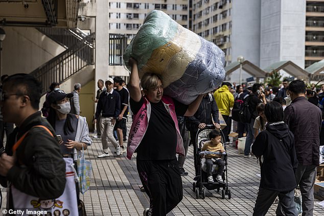 A man carries bedding near residential buildings that continue to burn at Wang Fuk Court in the Tai Po district on November 27, 2025 in Hong Kong, China