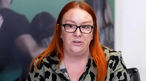 PA Media Charlotte Hennessy, the daughter of 29-year-old Jimmy Hennessy, with long red hair wearing black glasses and an olive green and black patterspeaking during a press conference
