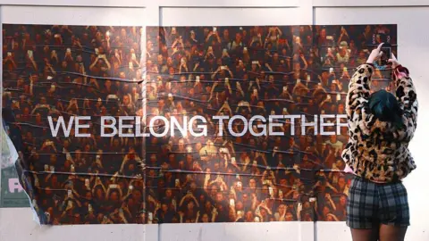 Getty Images A woman holds her phone camera up high above her head to take a photo of a Harry Styles 