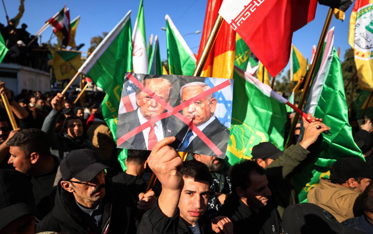A protester holds up crossed-out portraits of US President Donald Trump and Israeli Prime Minister Benjamin Netanyahu during a demonstration near the Iranian embassy in Baghdad on January 16, 2026, against Israel and recent US threats of military action in Iran, and in support of the Iranian regime and its supreme leader.