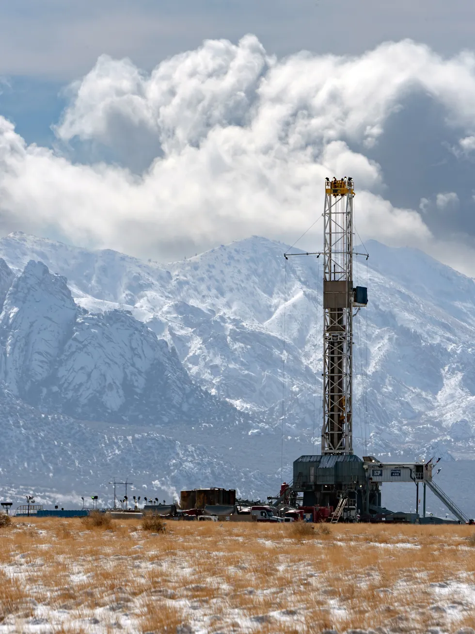 A geothermal drilling rig in a snowy prairie, with a large mountain range in the background.