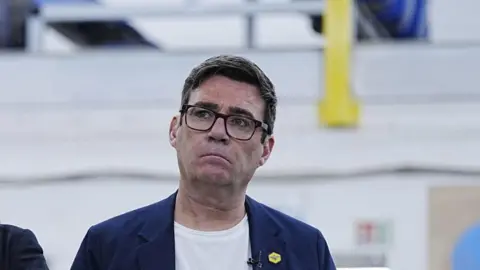 PA Media Headshot of Burnham who looks up and to the right. He has a serious expression. The background is blurry.