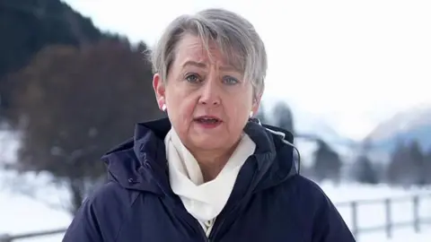 BBC Yvette Cooper speaking to BBC Breakfast from Davos, in Switzerland dressed in a blue winter coat and white scarf, against a snowy backdrop