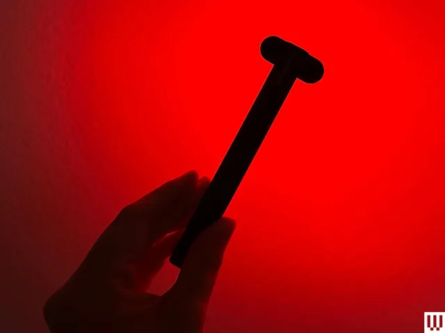 Hand holding the Solawave Radiant Renewal Want, a slender black device with red lights blaring from the oval top