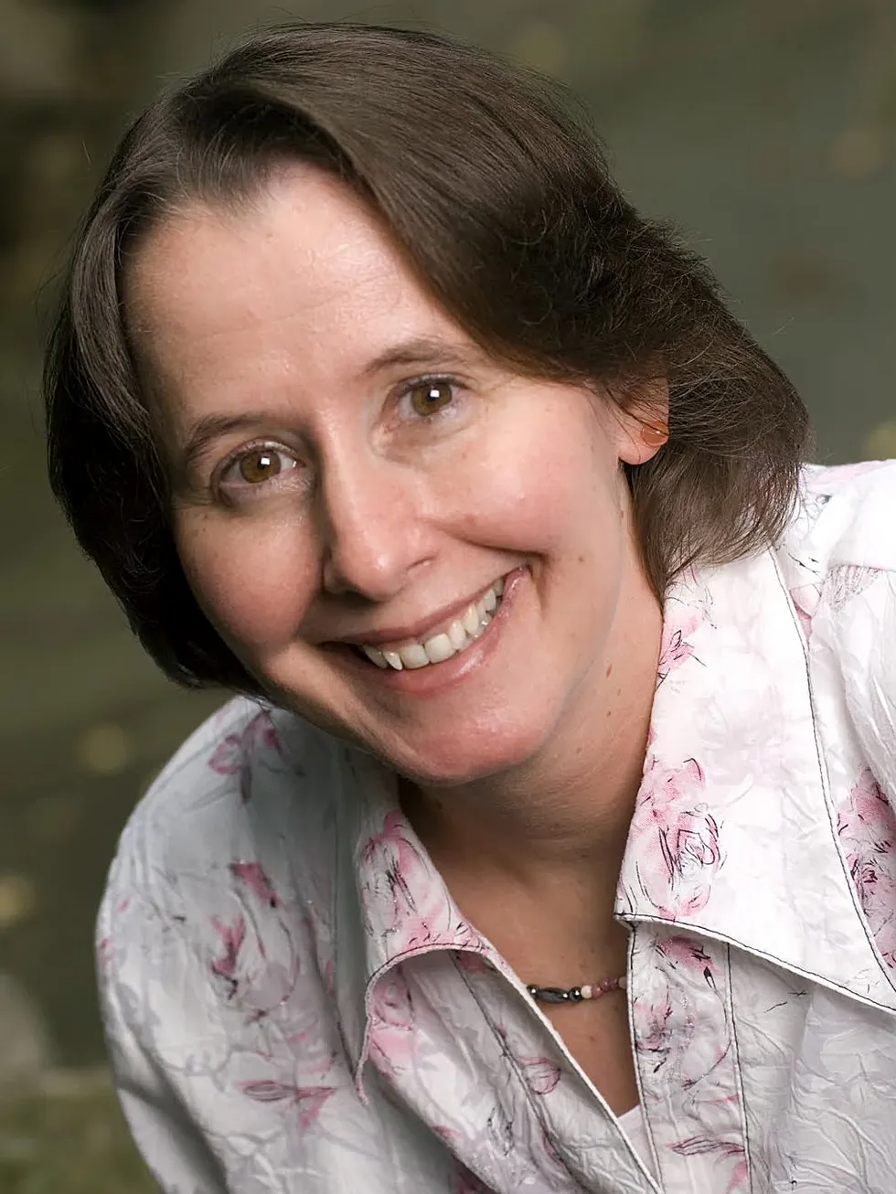 Person wearing a floral-patterned, white shirt and beaded necklace outdoors.